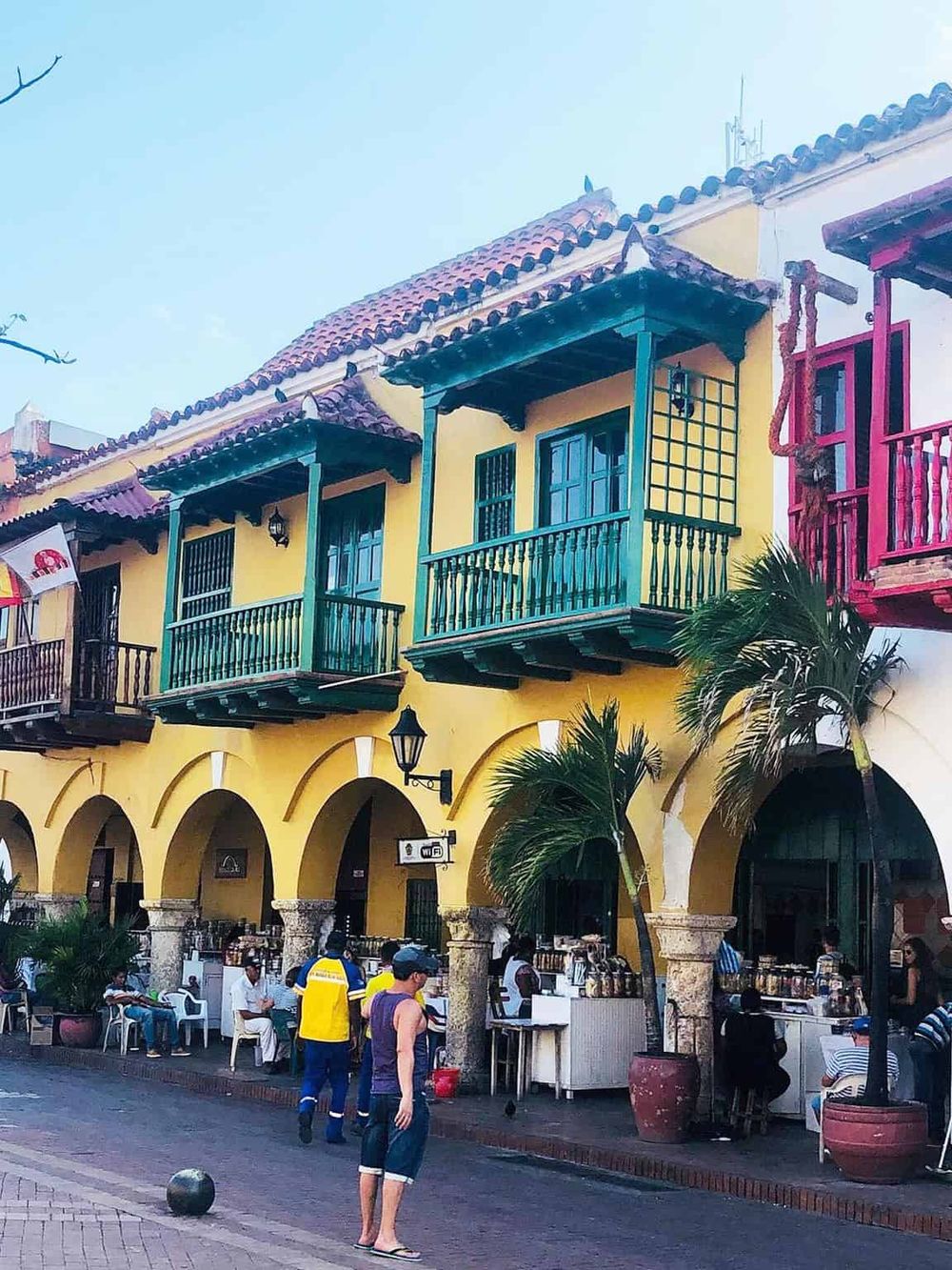 Colorful Mexican-style building with balconies and street vendors, highlighting vibrant architecture and local culture.