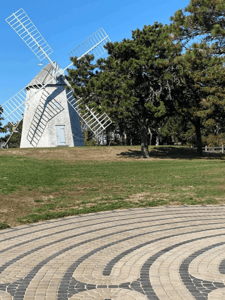 Old-fashioned windmill in a park surrounded by trees and a patterned brick walkway.