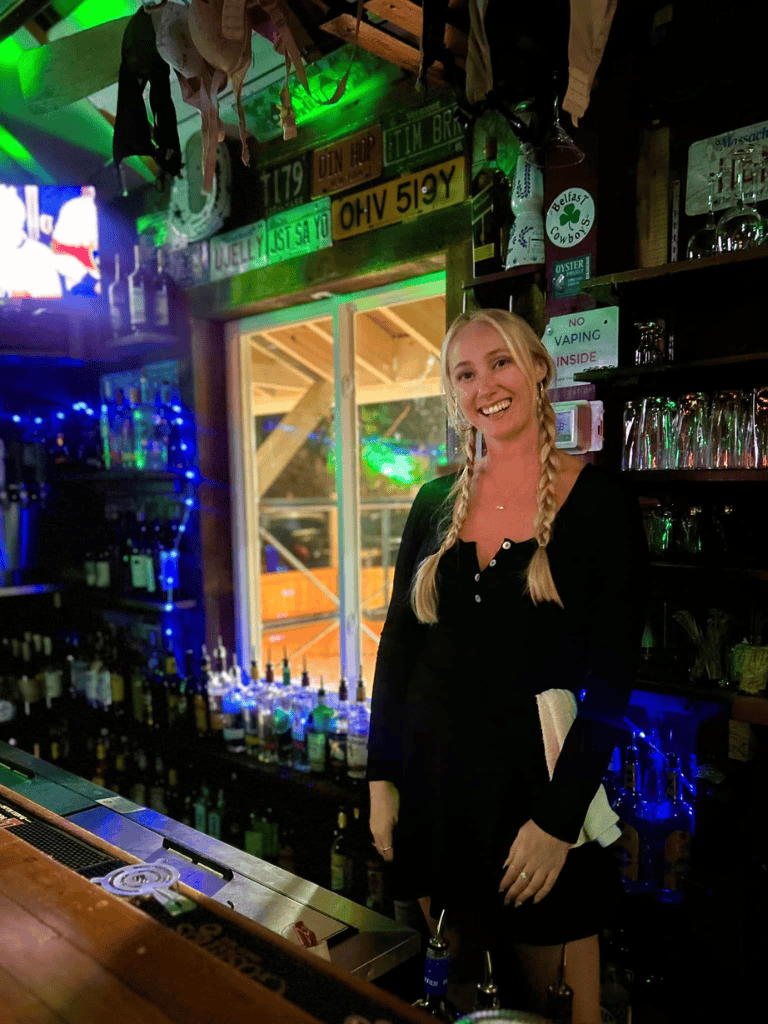 Bright bar scene with smiling bartender at QuestForDirections venue, vibrant neon lighting, and eclectic decor.