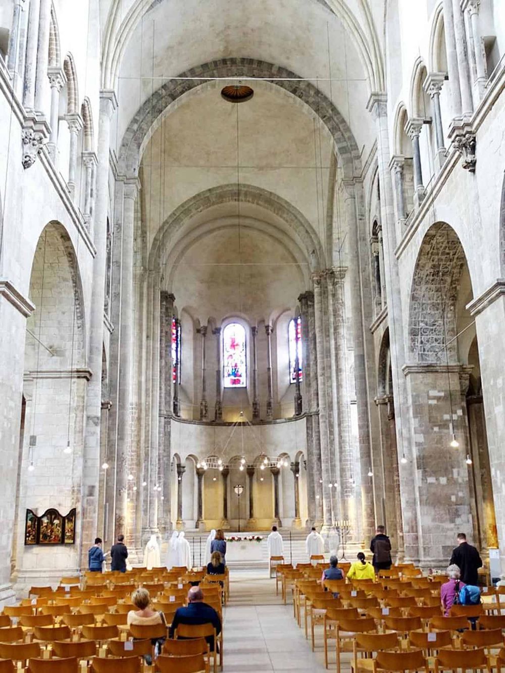 Ancient stone church interior with high vaulted ceilings, stained glass windows, and a small congregation attending a service.