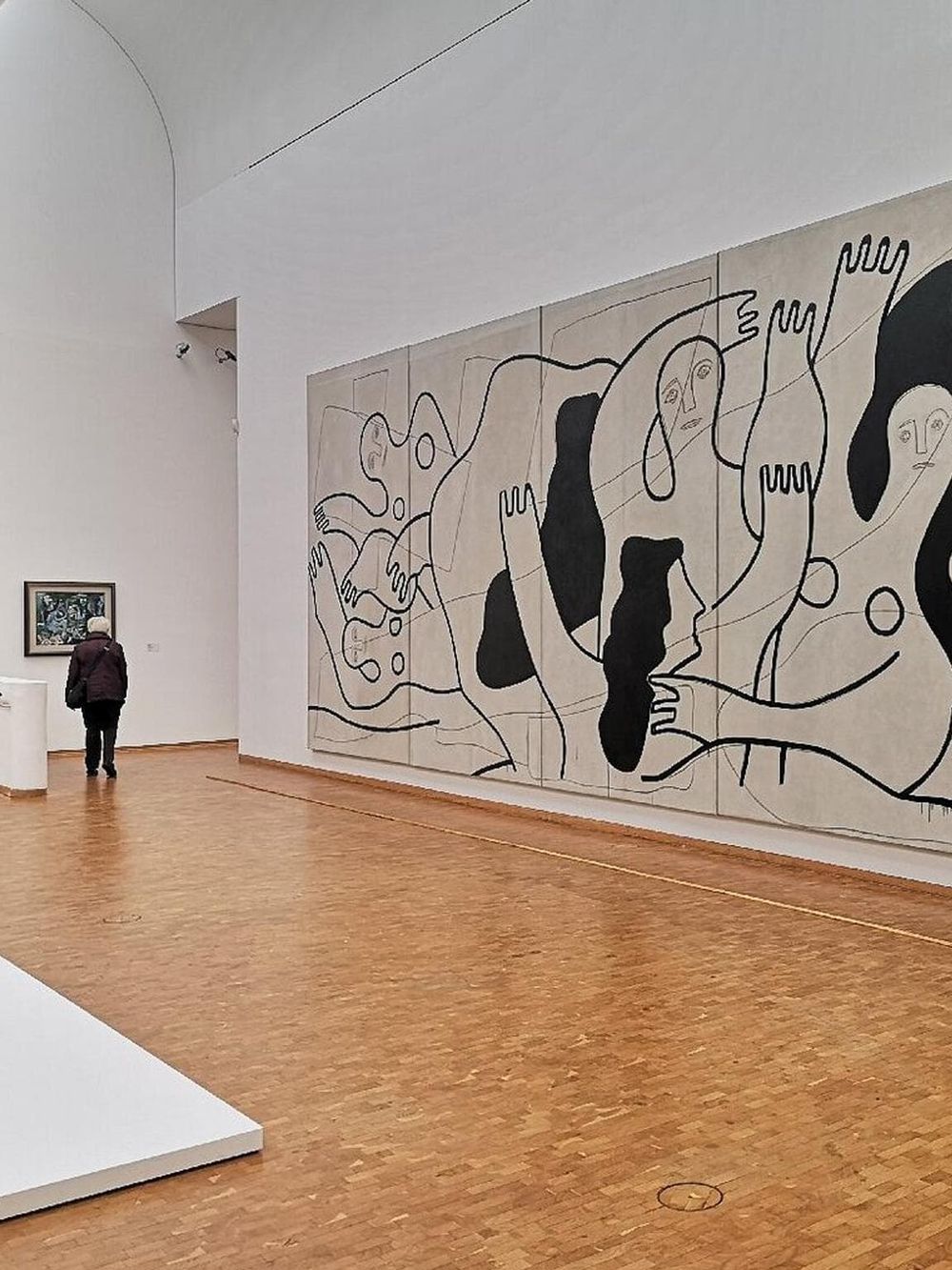 Contemporary art museum interior with large abstract mural and visitor exploring artwork.