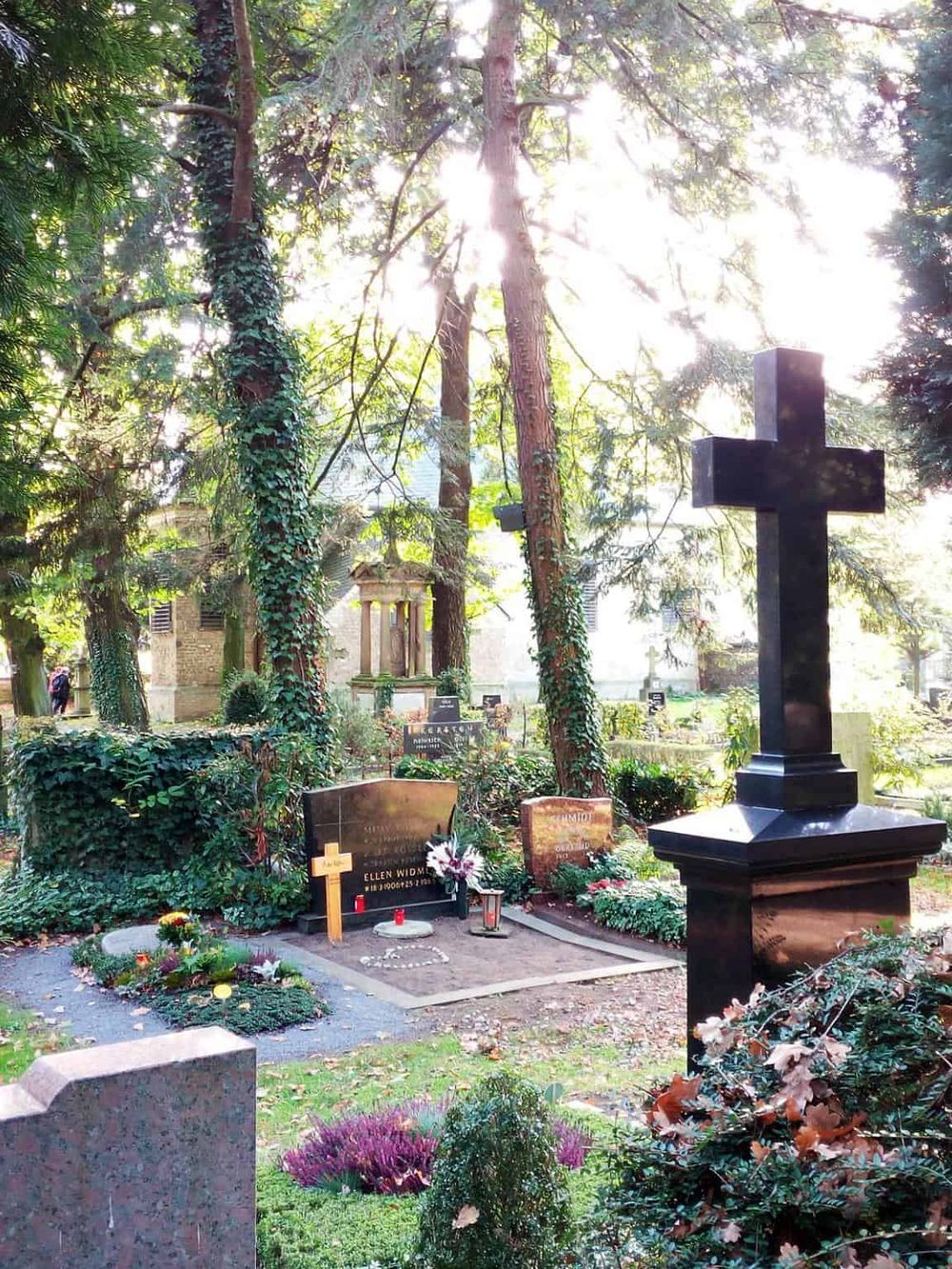 Sunlit cemetery with crosses, headstones, and lush greenery in a peaceful memorial garden.