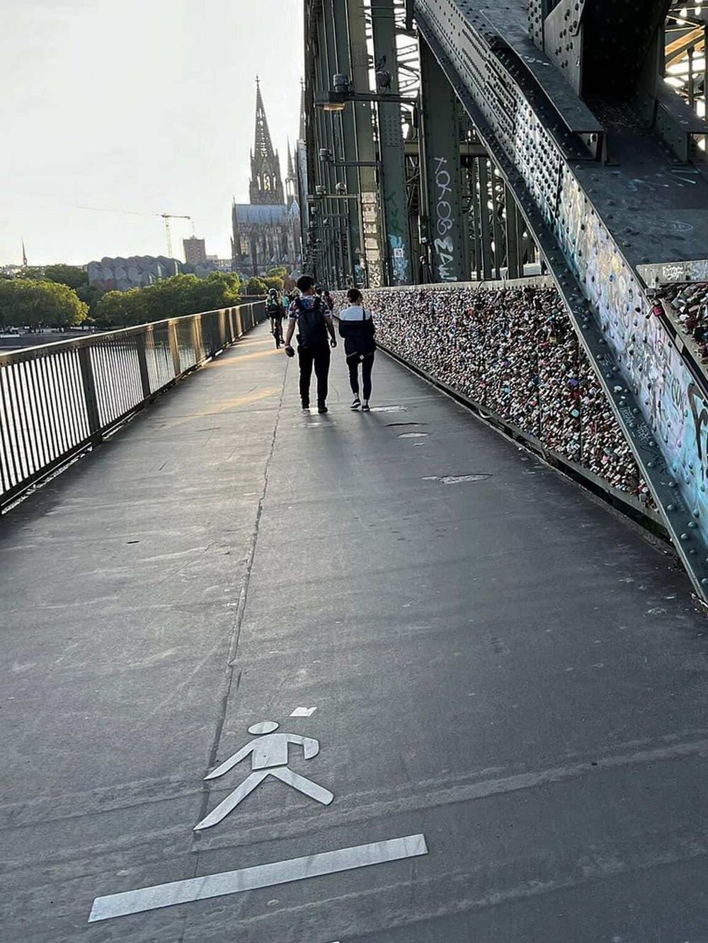 Pedestrian walkway on a bridge with cityscape and Notre-Dame Cathedral in the background, featuring love lock railings.