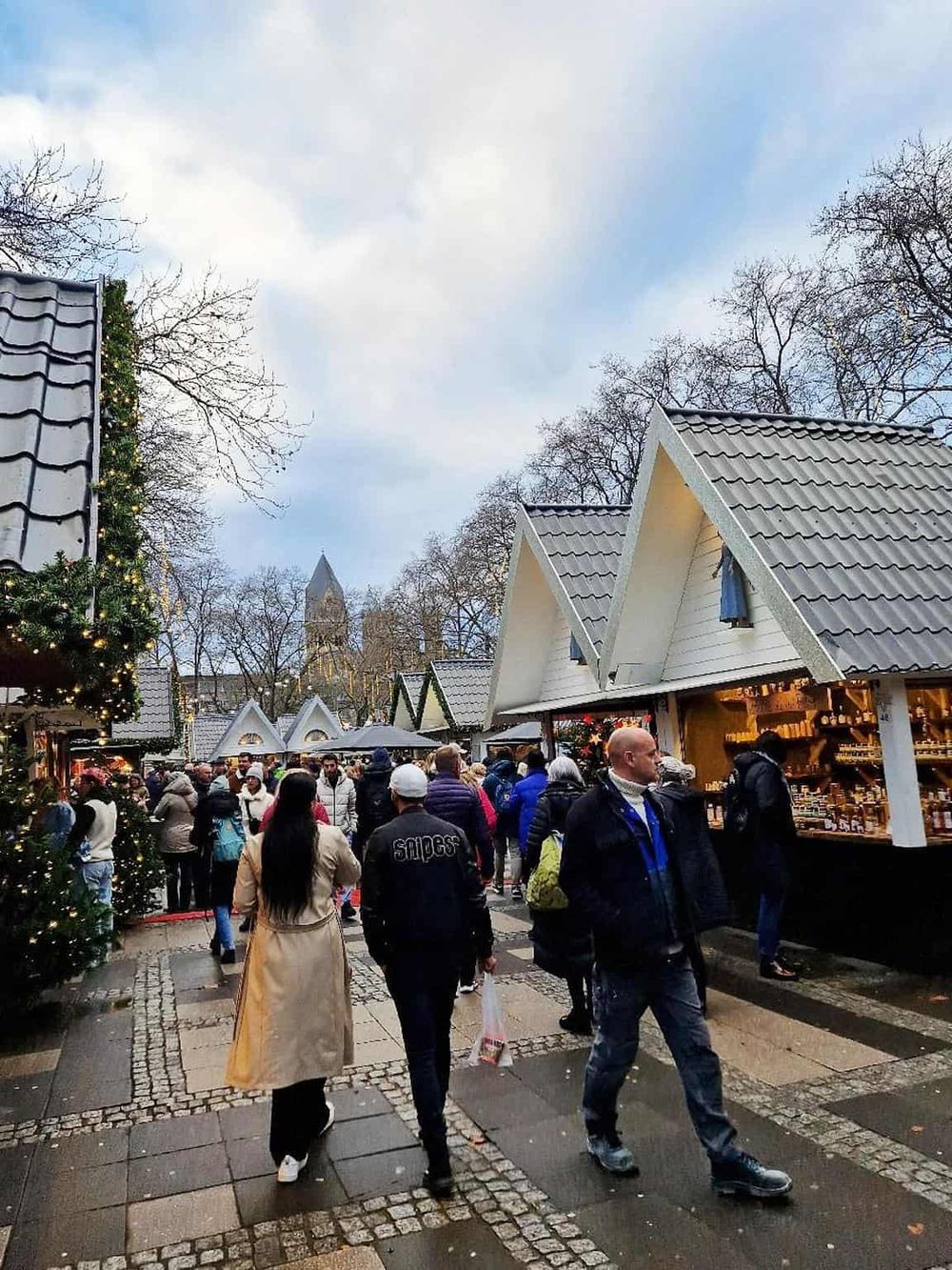 Vibrant holiday market scene with visitors shopping, festive decorations, and charming wooden stalls in a winter setting.