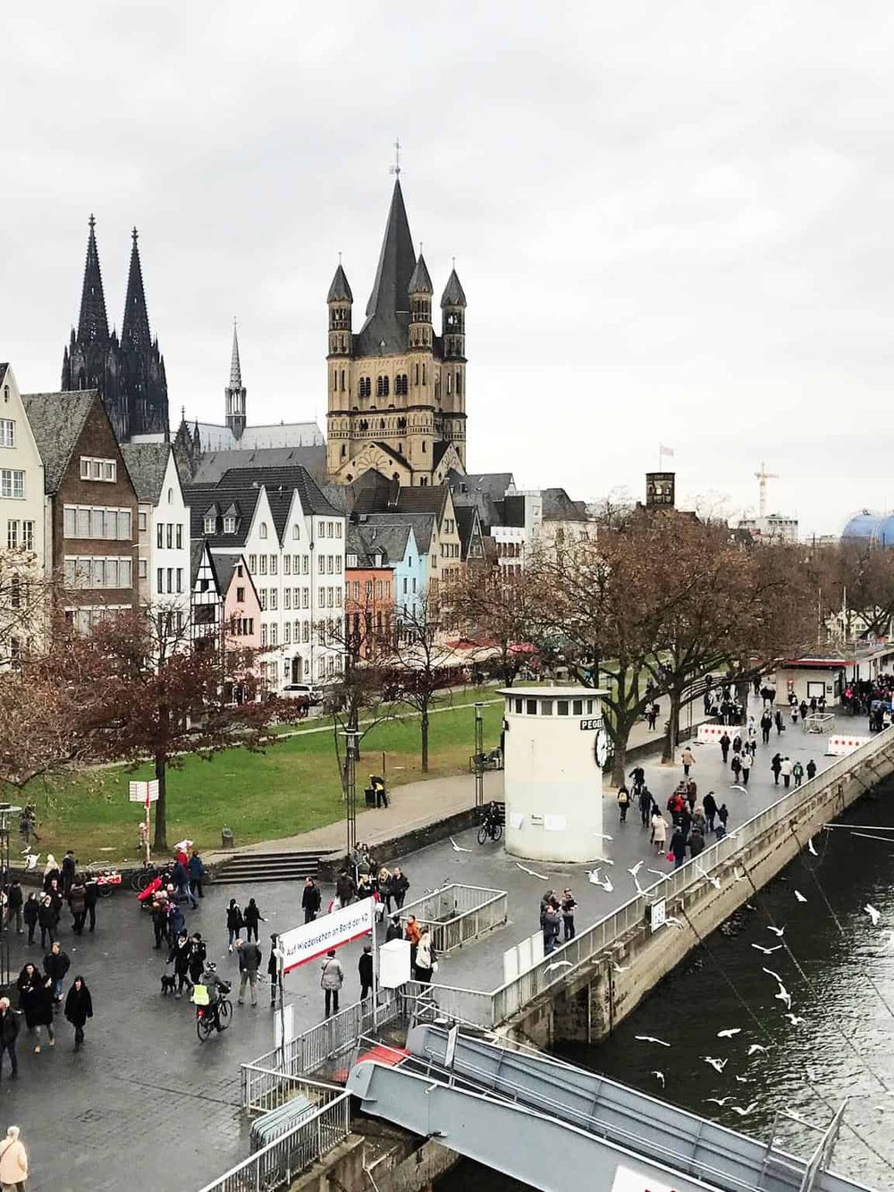 Historic Cologne Cathedral and scenic riverwalk in Cologne, Germany, with pedestrians enjoying the cityscape.