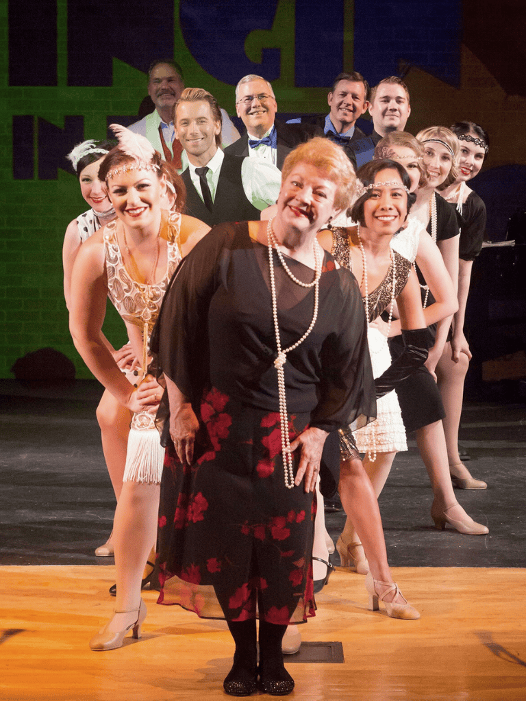 Elegant group of performers and a woman in vintage attire at QuestForDirections event on stage.