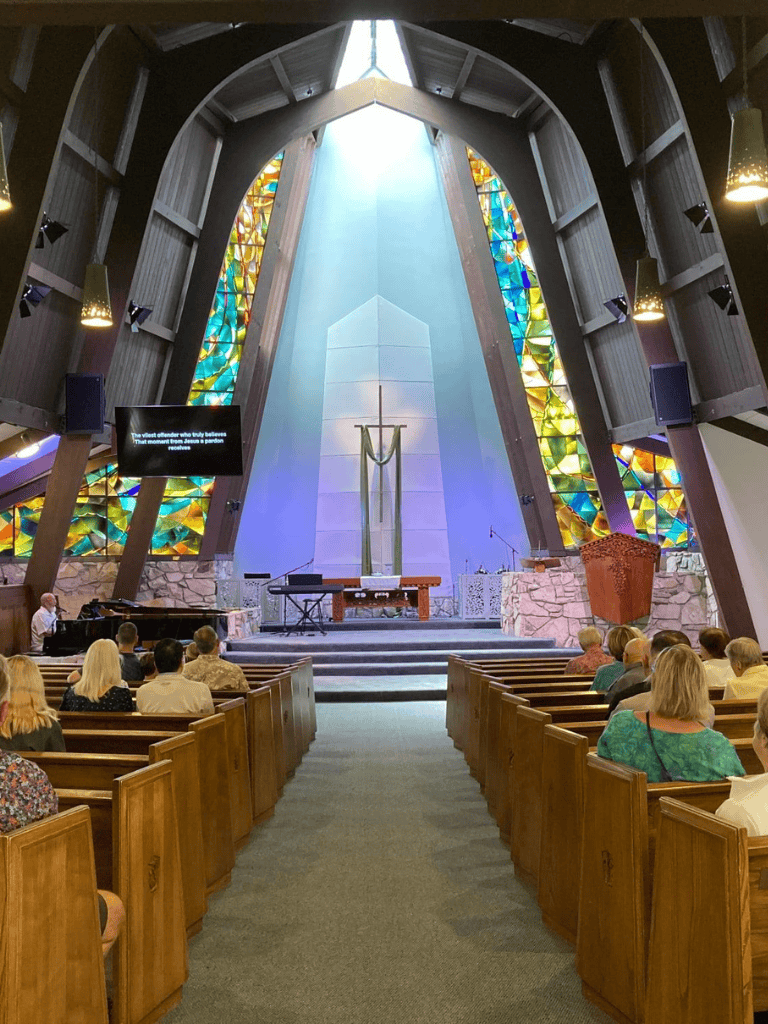 Colorful stained glass windows in a modern church interior with congregation and altar.