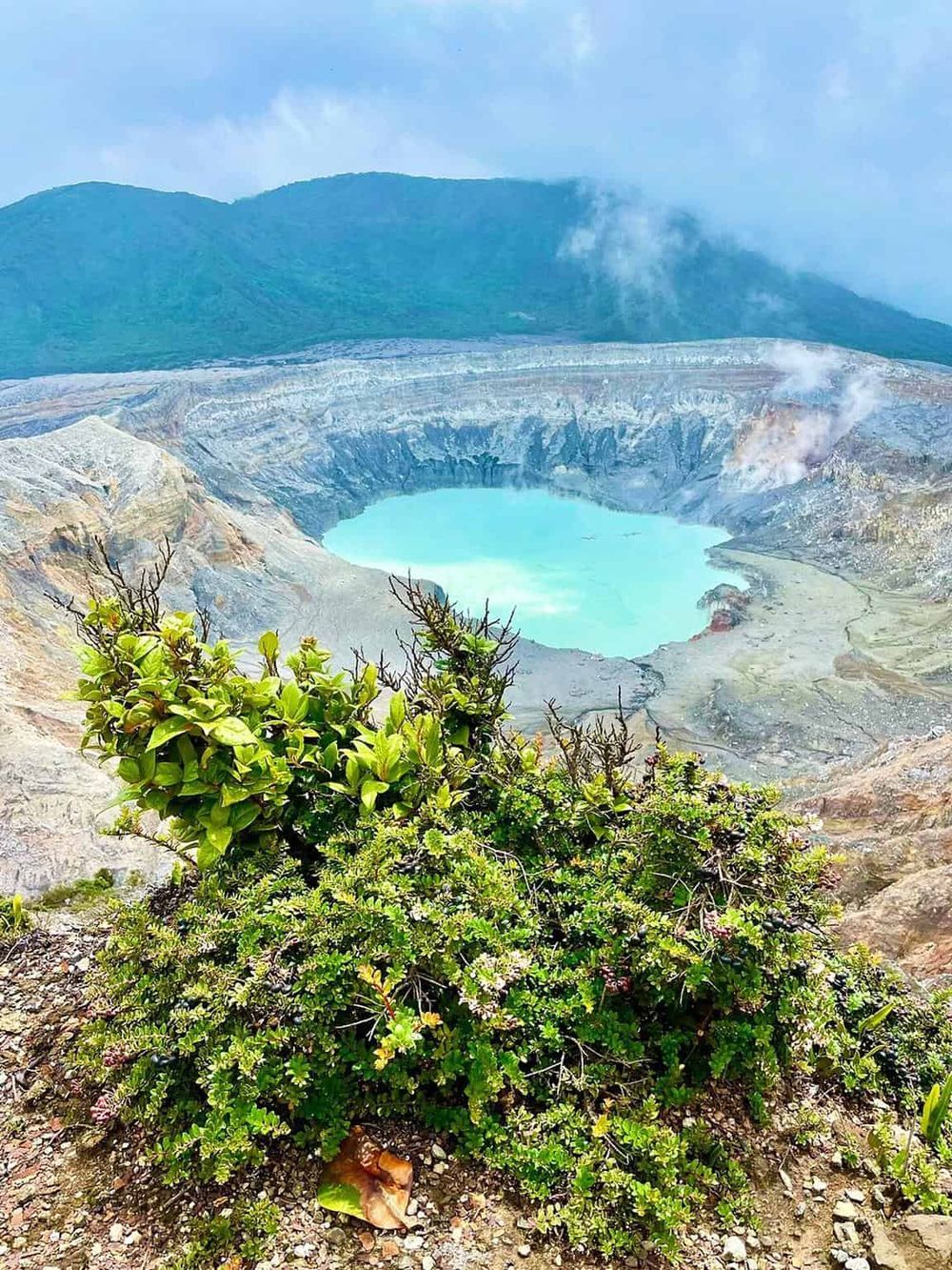 Vulcano crater lake with turquoise waters, surrounded by volcanic ash, lush greenery, and scenic mountain views.