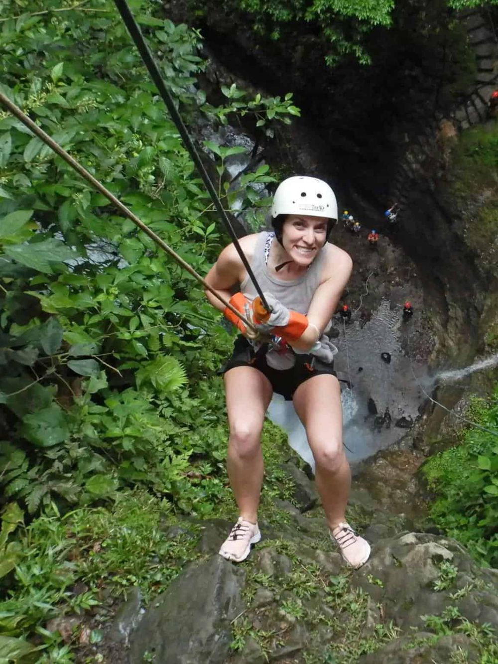 Adventurous woman canyoning in lush green forest, wearing helmet and harness.