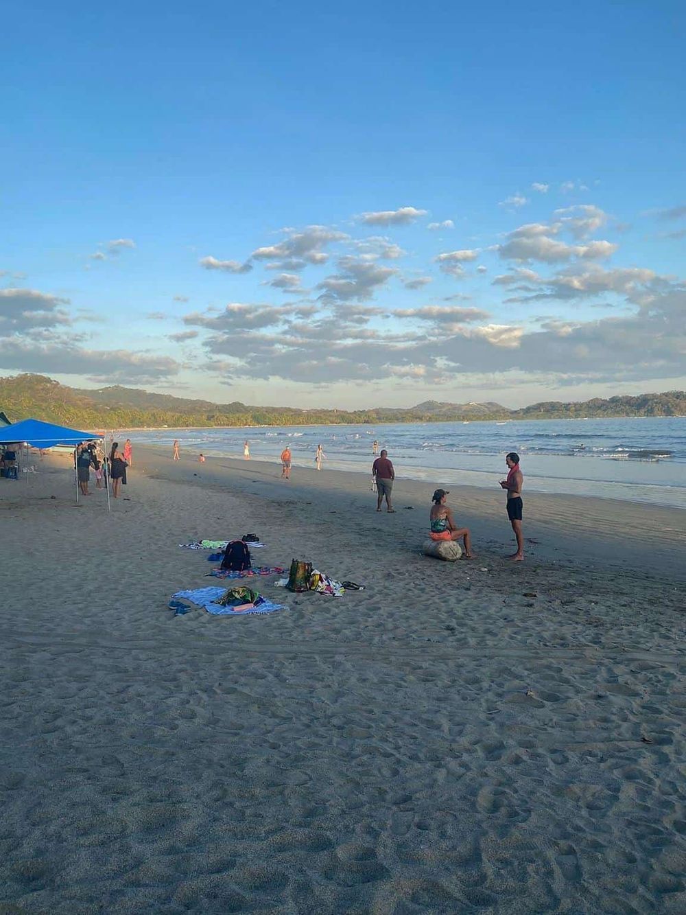 Scenic beach with people enjoying sunset, gentle waves, and clear sky, perfect for relaxing and beach activities.