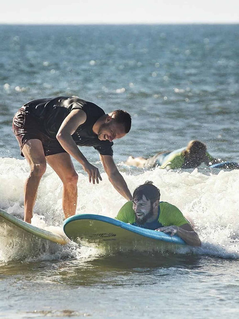 Surfer helping a beginner on the waves for an adventure-filled day at the beach.