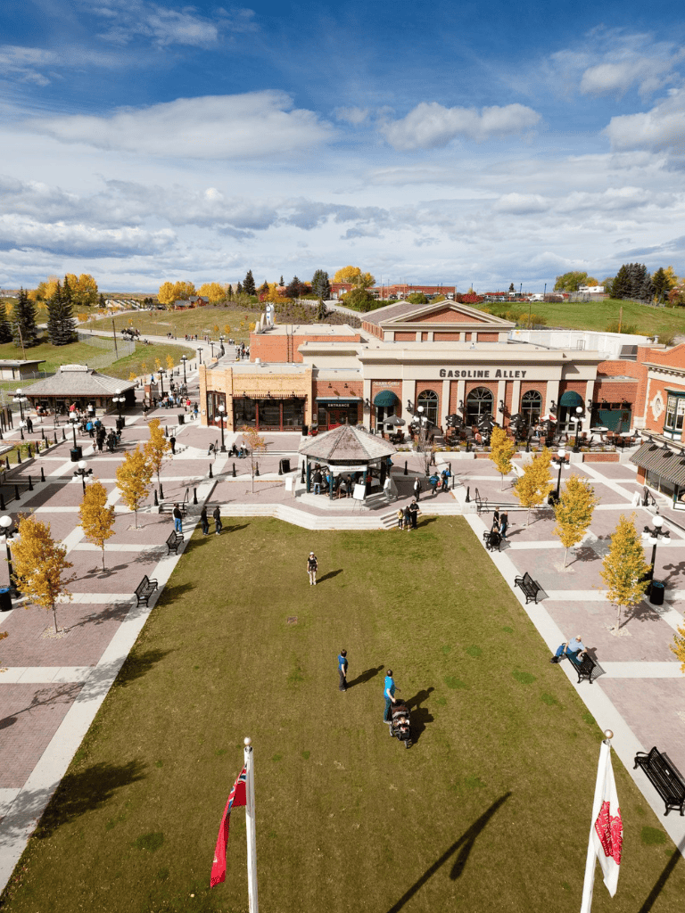 Vibrant outdoor shopping plaza with Gasoline Alley stores, autumn trees, and visitors enjoying a sunny day.