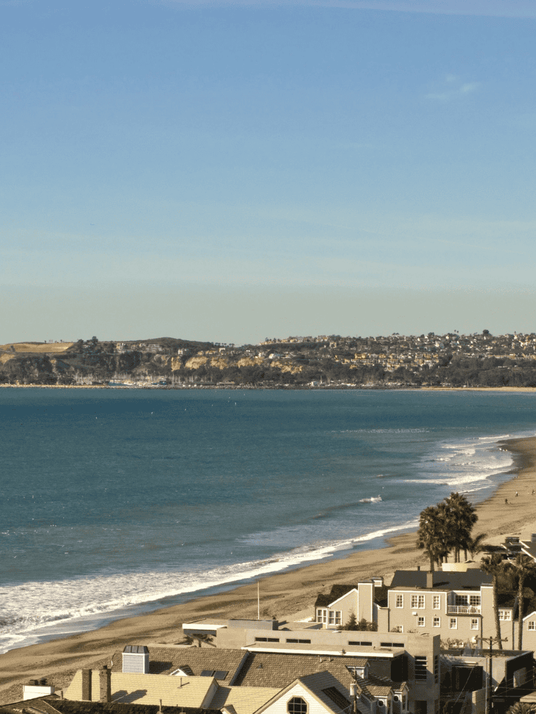 Vibrant coastal scenery with sandy beach, ocean waves, and residential homes overlooking the sea.