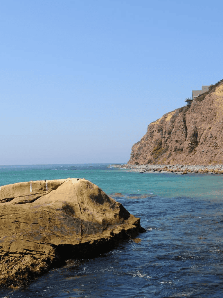 Pristine coastal scenery with rocks, cliffs, and ocean waves under a clear blue sky.