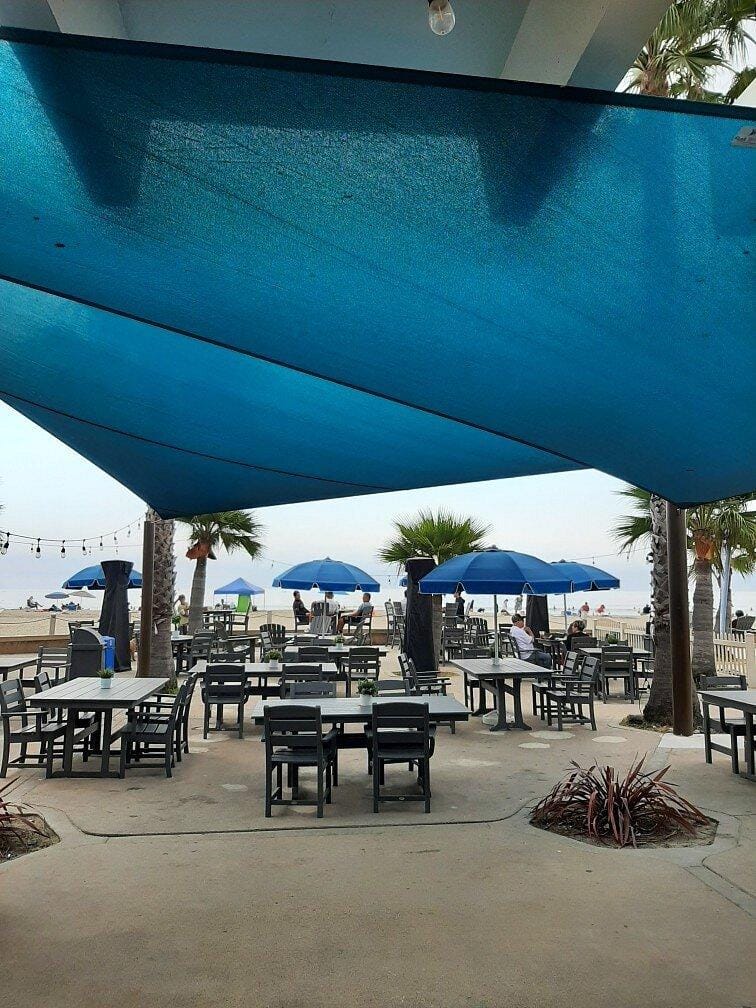 1. Outdoor beachside dining area with umbrellas and shaded seating under blue sunshade.