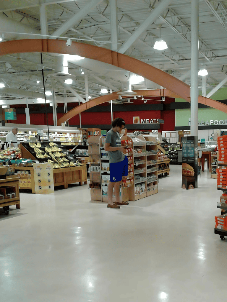 1. A shopper in a grocery store browsing snacks and produce aisle, shopping for fresh food.