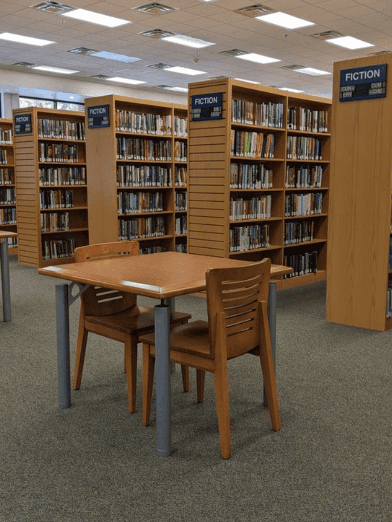 Fiction section in a library with wooden bookshelves and reading table.