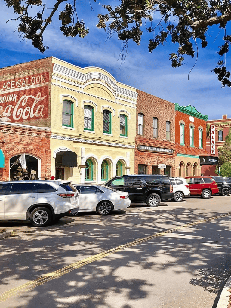 Colorful historic buildings on a city street with parked cars and tree shadows, a charming downtown scene.
