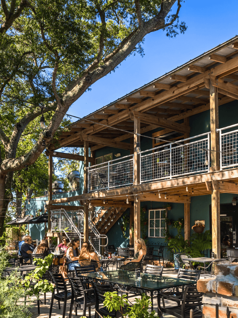 Vintage outdoor restaurant with blue walls, wooden balcony, and lush greenery.