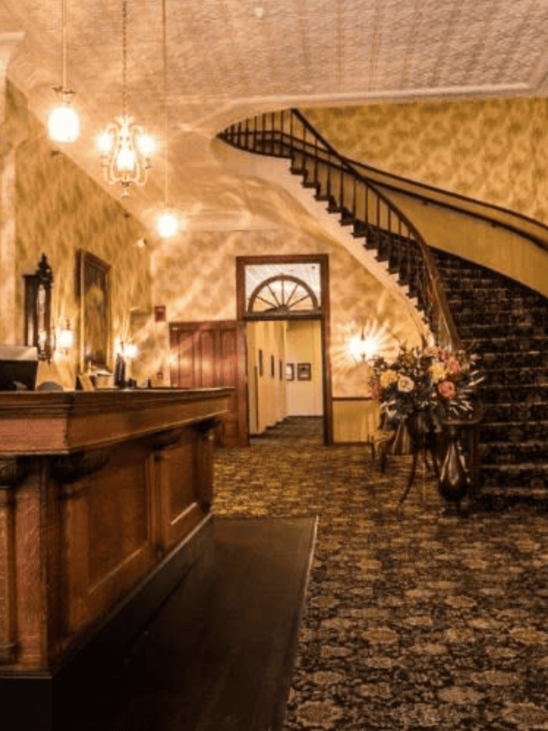 Elegant hotel lobby with staircase, wooden accents, floral arrangement, and warm lighting for welcoming guests.