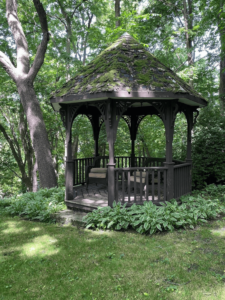 Quaint black wooden gazebo in lush green garden for peaceful outdoor relaxation.