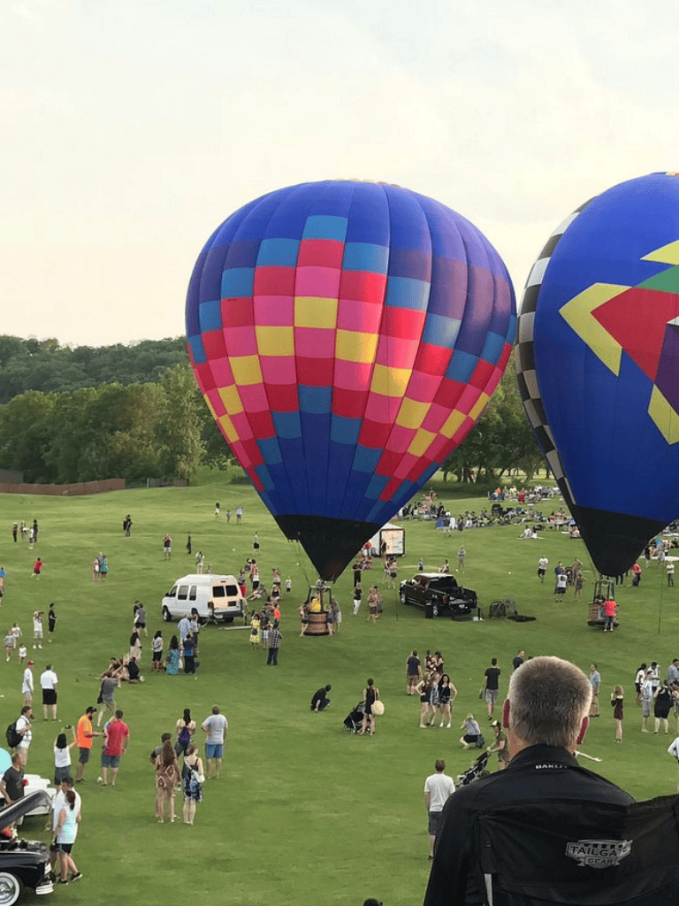 Colorful hot air balloons at outdoor festival with crowd and scenic background.