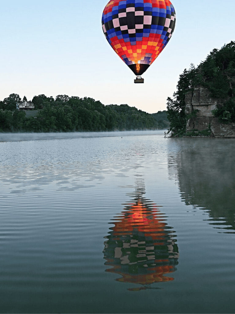 Colorful hot air balloon soaring over a serene river at dawn.