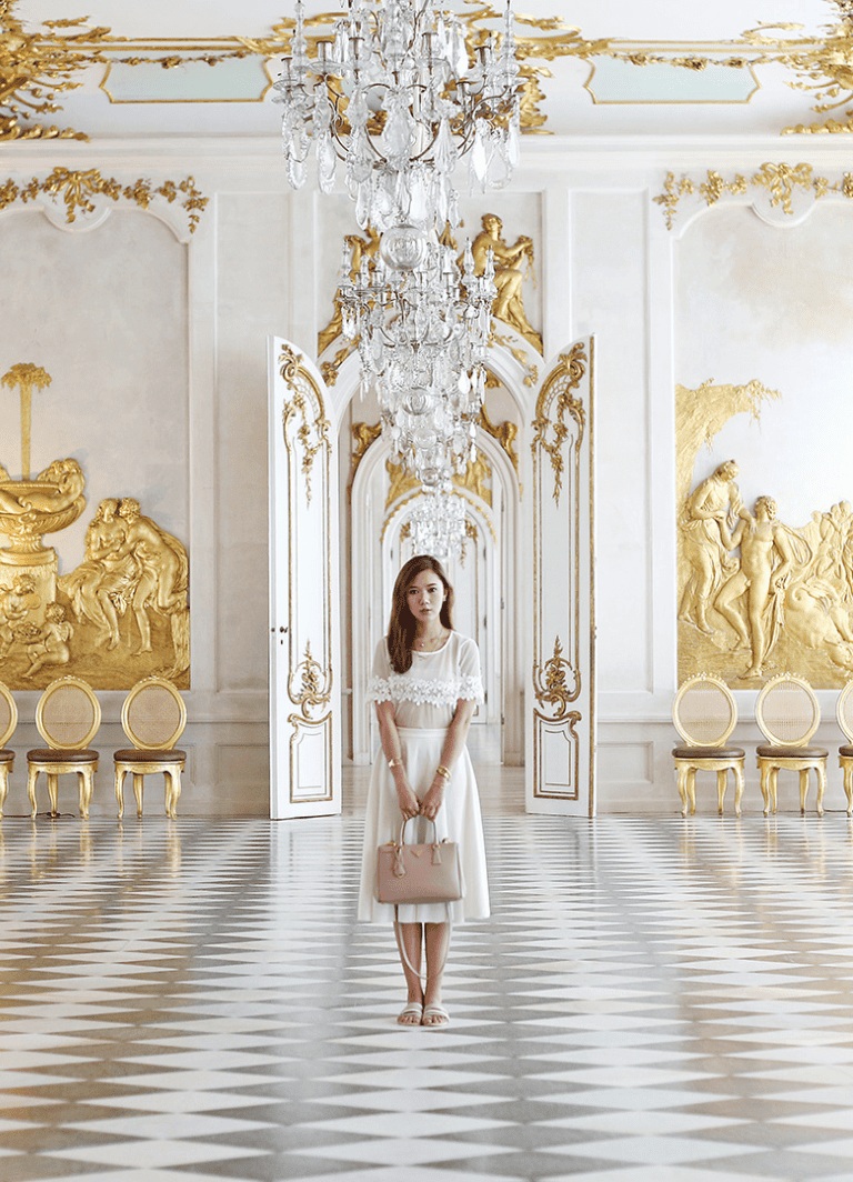 Luxurious palace interior with crystal chandelier, gold accents, and elegant woman in white dress.