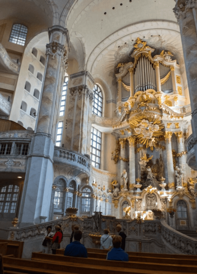 Opulent Baroque church interior with gold accents, elaborate sculptures, and soaring architecture.