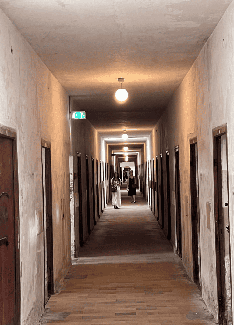 Old hotel corridor with worn walls and wooden doors, dim lighting, and a vintage ambiance.
