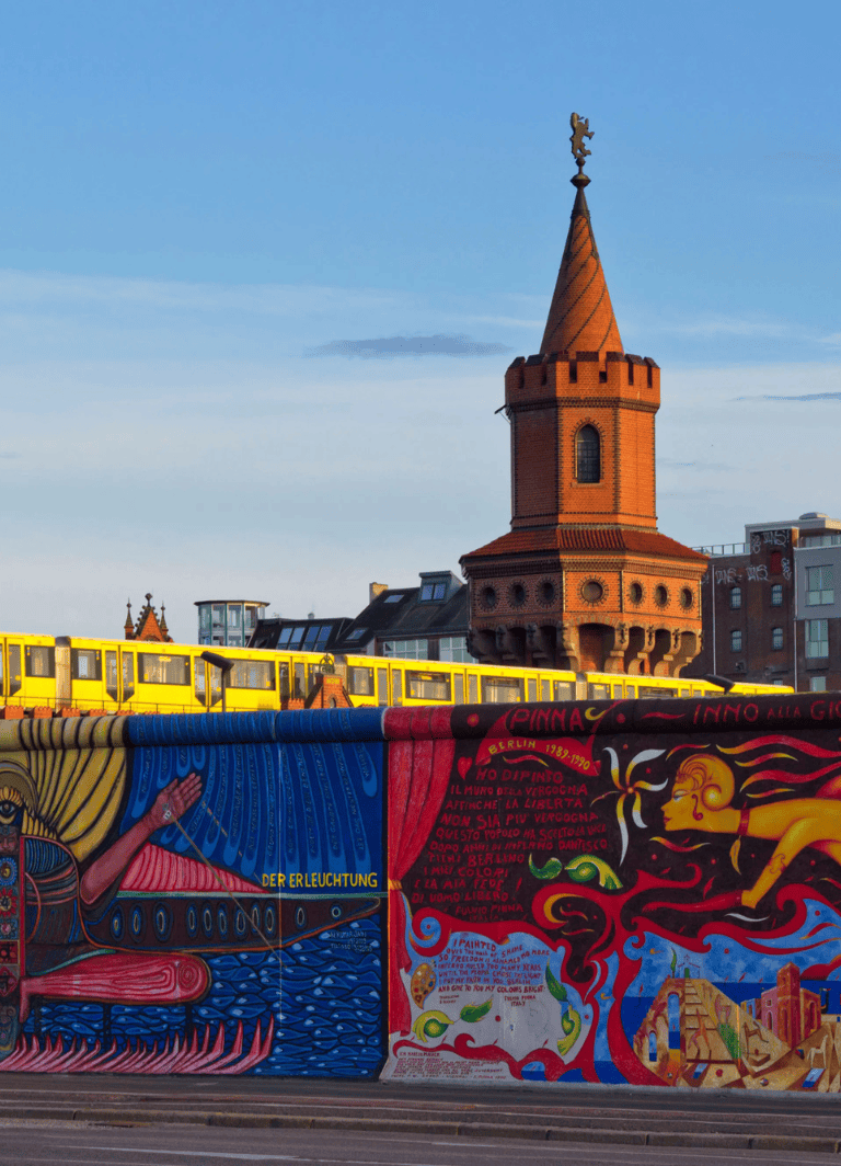 Berlin mural art with historic tower and yellow train in the background, showcasing vibrant street art and city architecture.