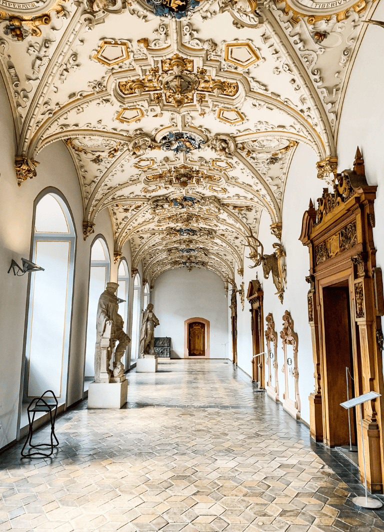 Intricate Baroque ceiling in historic palace hallway with sculptures and ornate woodwork.