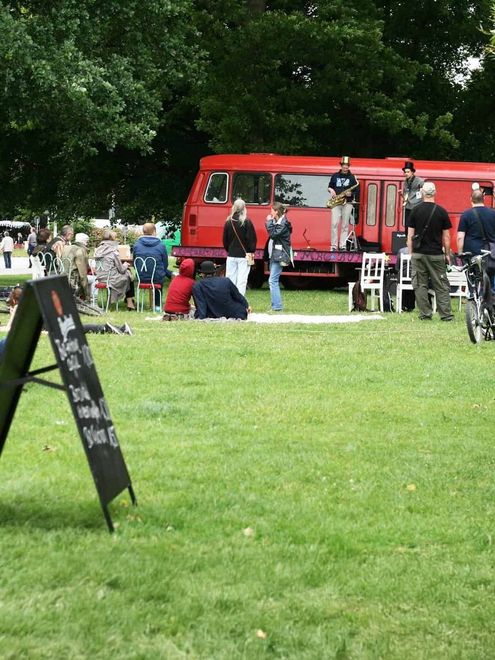 Vintage red bus transformed into a pop-up music stage with a live street performance in a park.