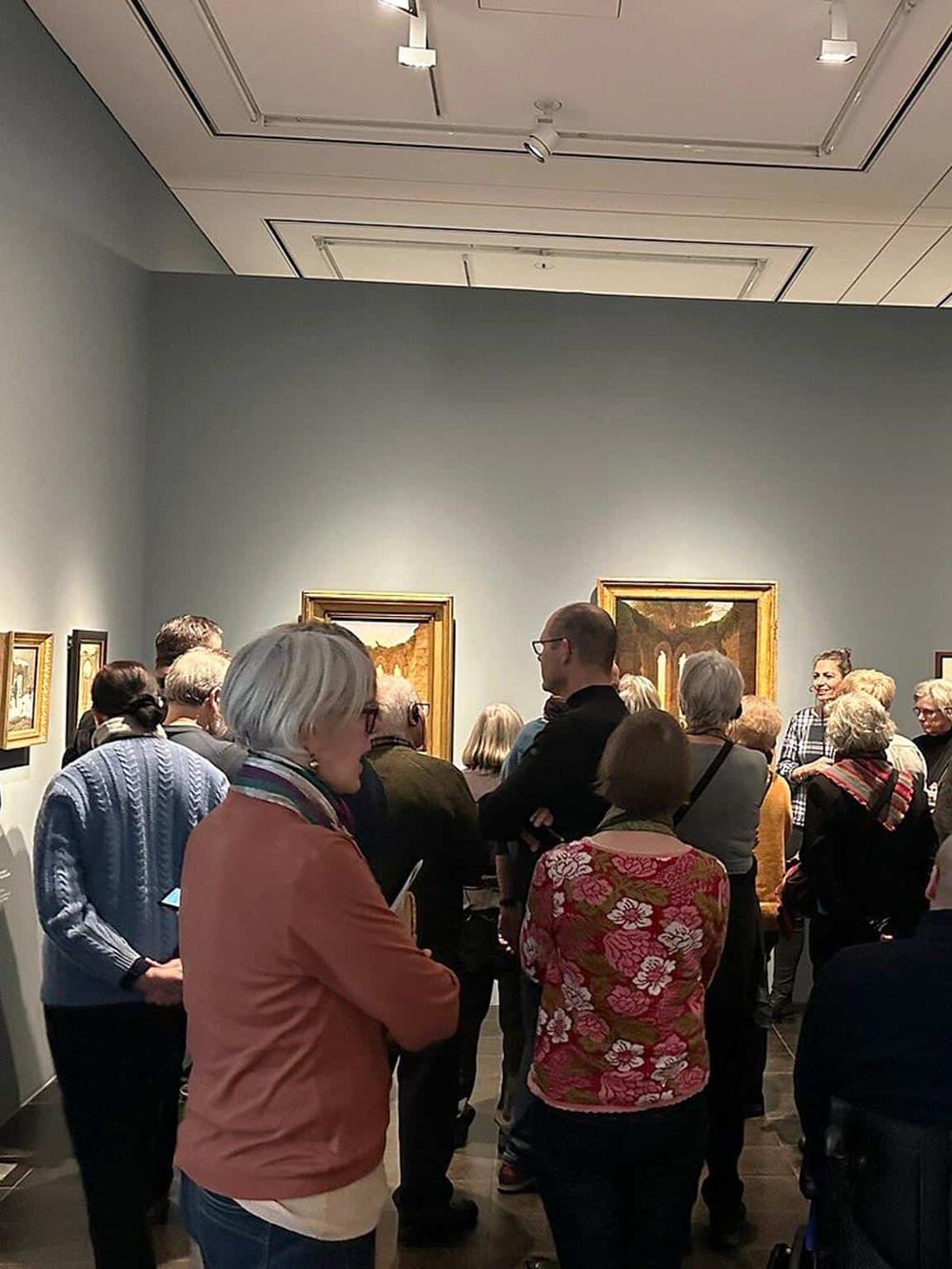 Busy art gallery with people observing framed paintings, showcasing art appreciation and cultural engagement.