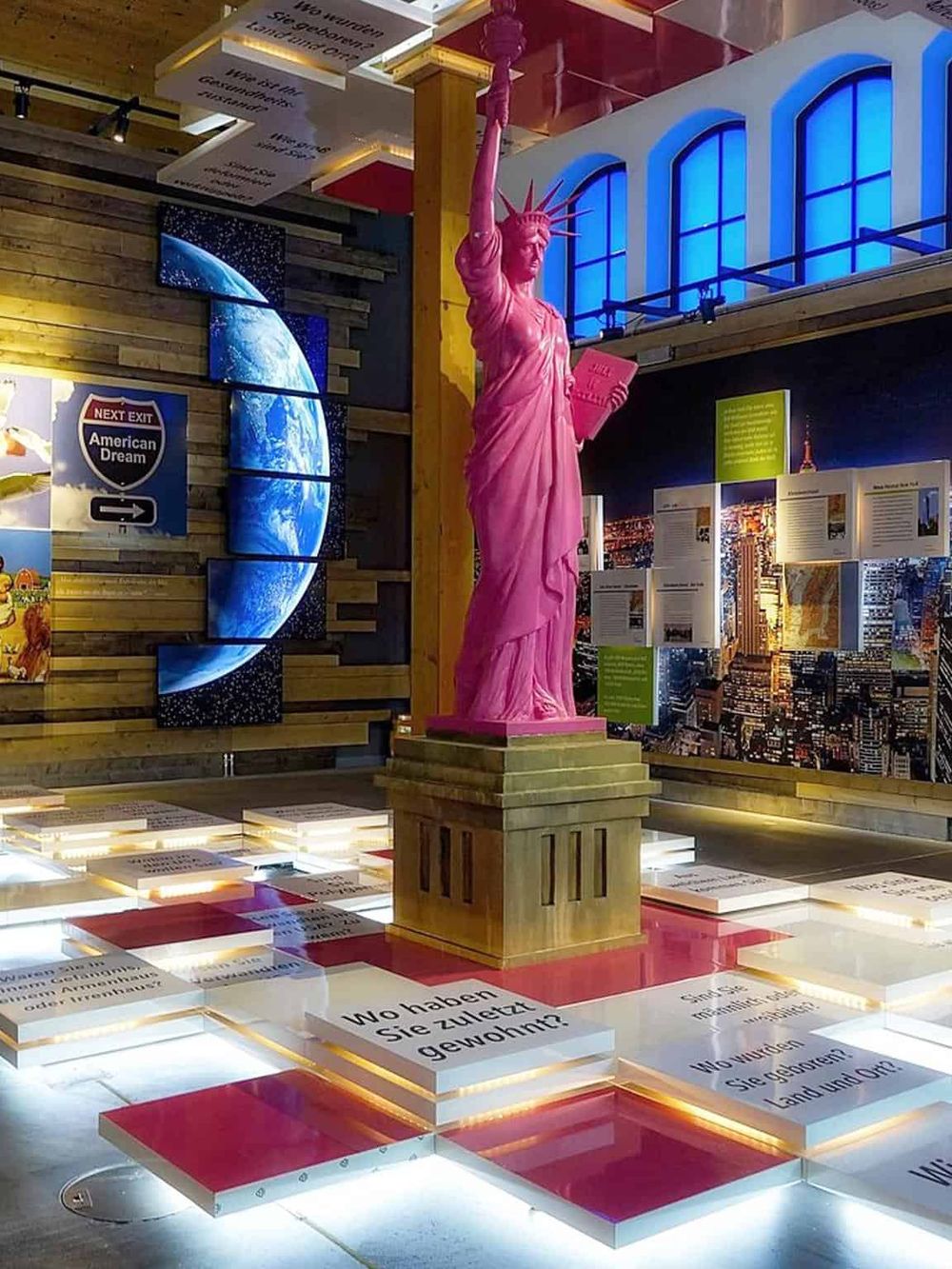 Statue of Liberty replica inside an interactive museum exhibit with educational displays and digital maps.