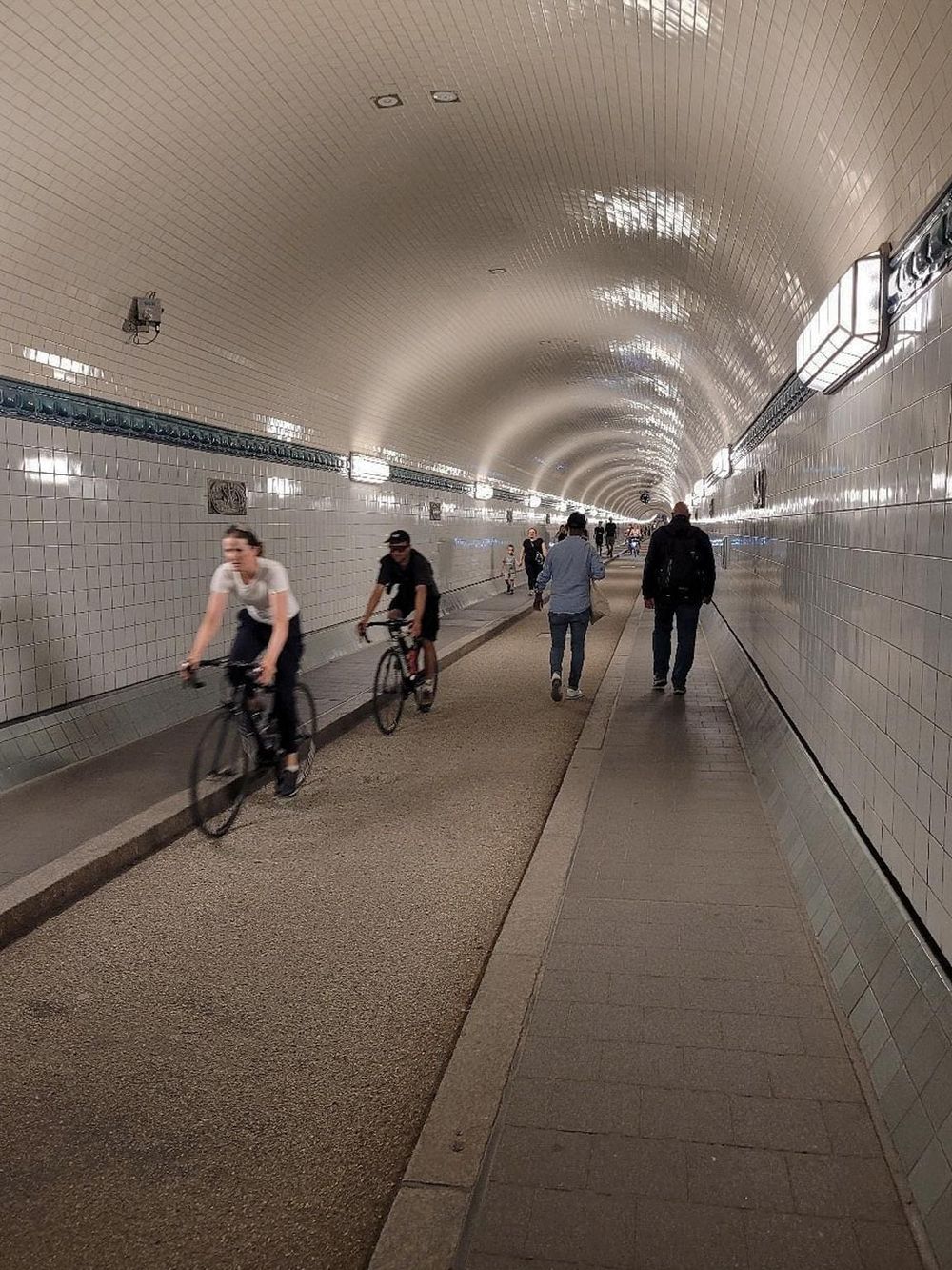 Underground tunnel with pedestrians and cyclists, illuminated ceiling, urban transit pathway.