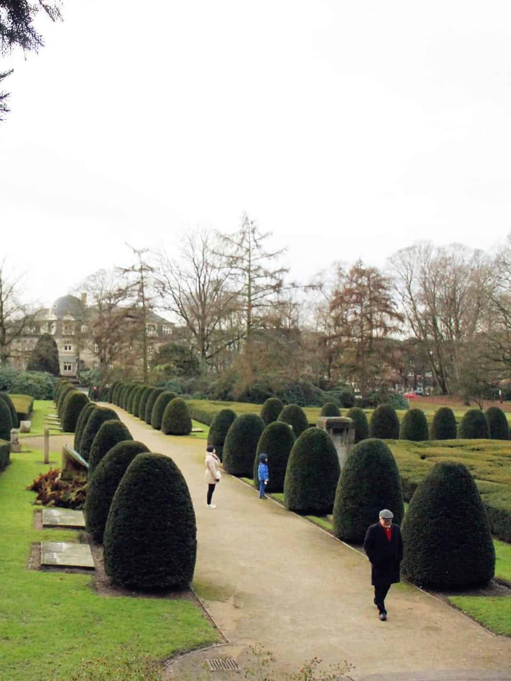 Well-maintained formal garden with trimmed bushes and visitors walking along scenic pathways.