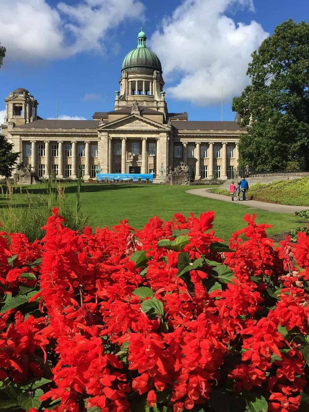 Historic government building with green dome, surrounded by vibrant red flowers and green trees.