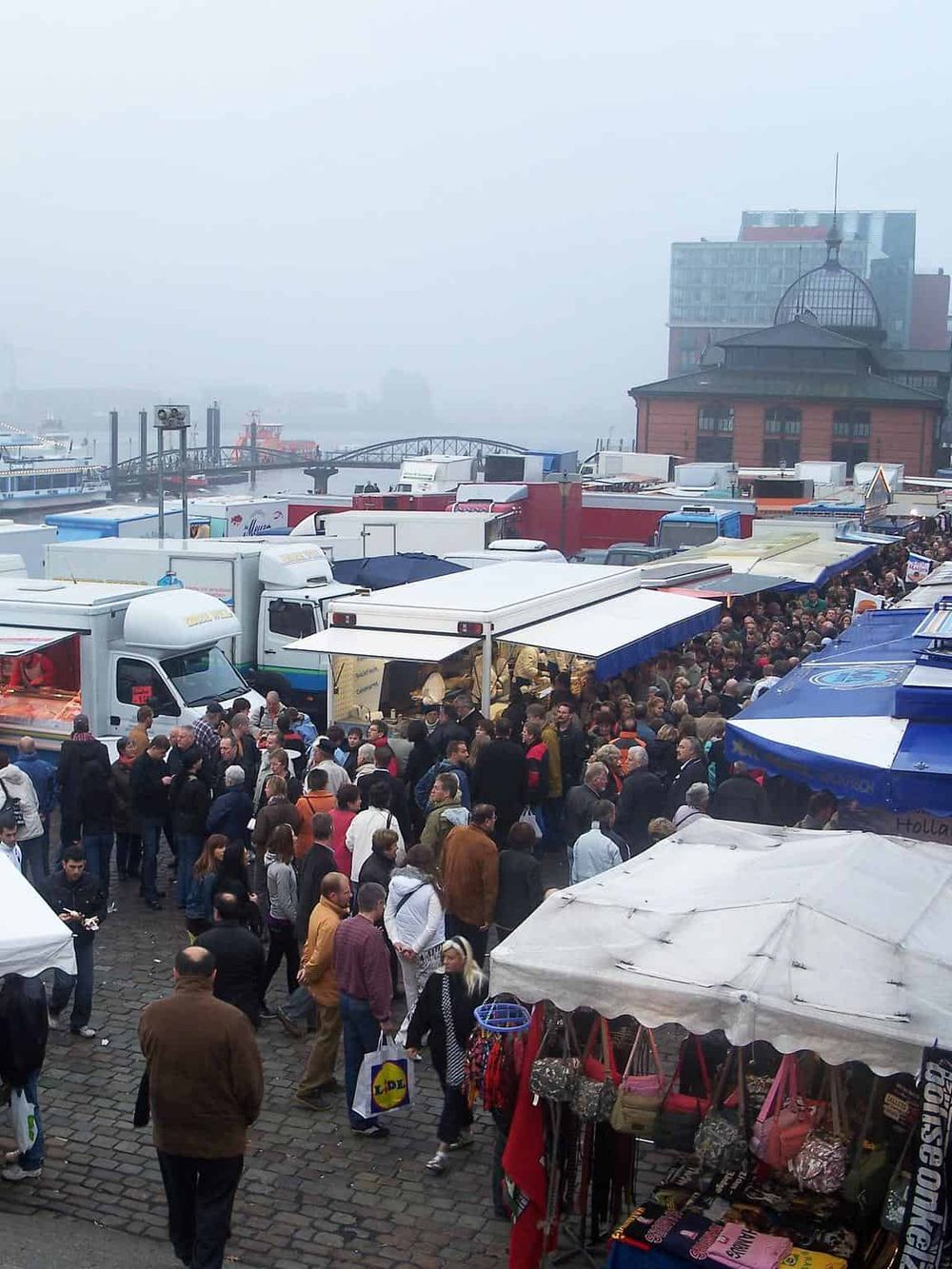 Crowded food truck market at the waterfront, featuring diverse vendor stalls and visitors enjoying outdoor dining.
