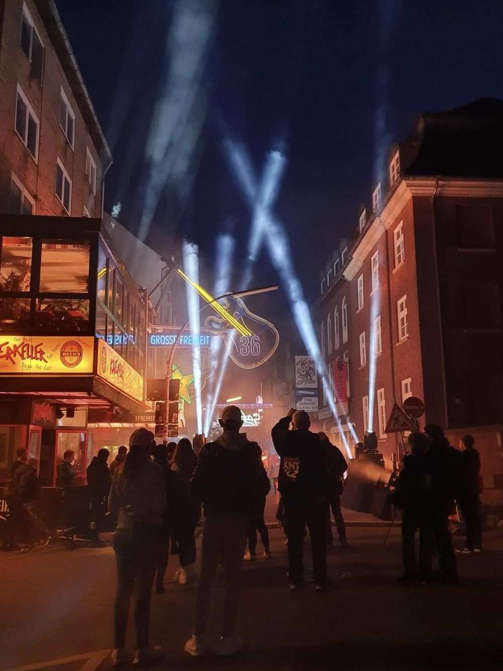 Bright night scene with energetic crowd and vibrant beams of light in an urban nightlife setting, showcasing event entertainment and city life.