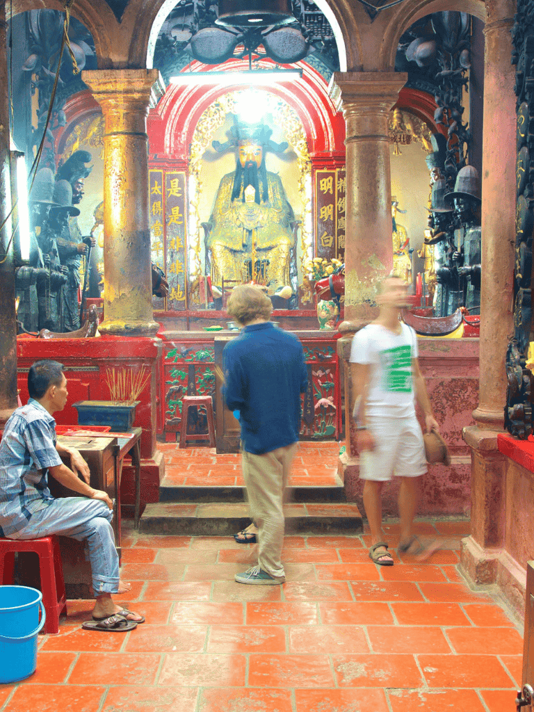 Ancient Chinese temple interior with worshippers and a regal deity statue, rich in cultural symbolism and vibrant colors.
