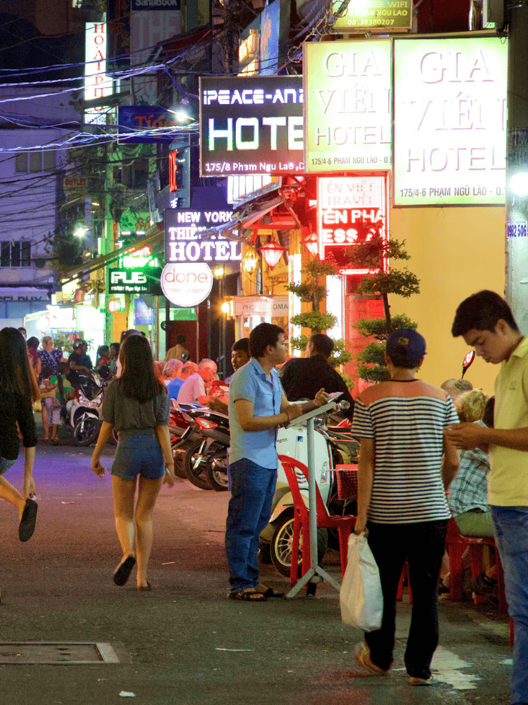 Night street scene with neon signs, busy pedestrians, and scooters in Vietnam, highlighting urban nightlife and local commerce.