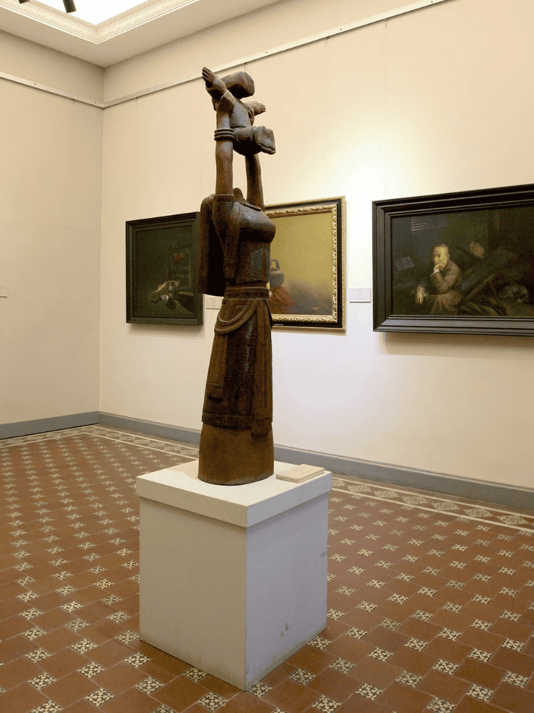 Traditional African wooden sculpture featuring geometric motifs and cultural symbolism, displayed in an art gallery.