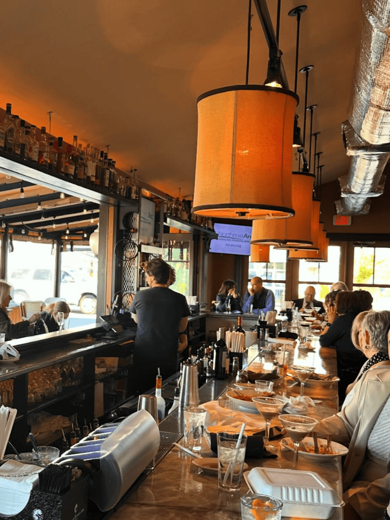 Cozy bar and restaurant interior with patrons enjoying drinks and conversation, modern design, warm lighting, and inviting atmosphere.