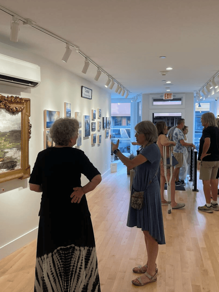 - Diverse group of people viewing artwork at QuestForDirections art gallery in a well-lit space.