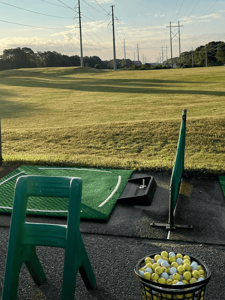 Driving range with golf balls and hitting mats overlooking lush green fairway and power lines, ideal for golf practice and improvement.