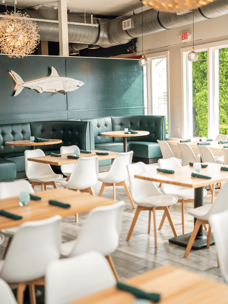 Shark wall art in modern restaurant, stylish dining area with white chairs and wooden tables, natural light, contemporary decor.