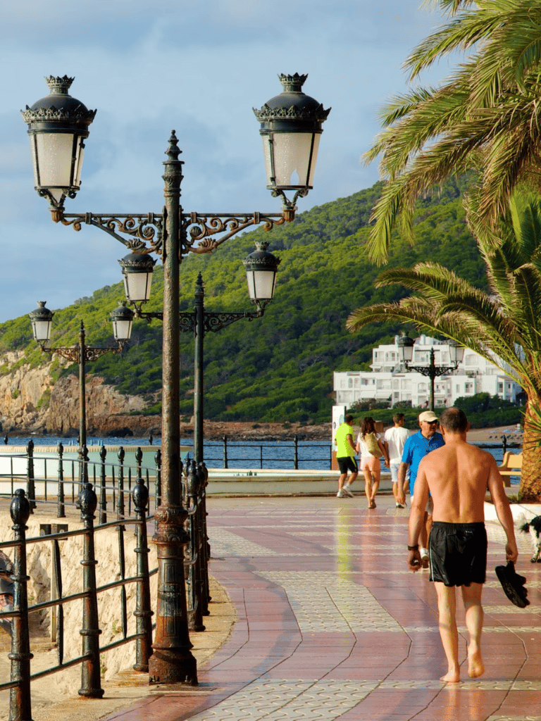 Bright seaside promenade with vintage lampposts, palm trees, and beachside walkers in QuestForDirections.