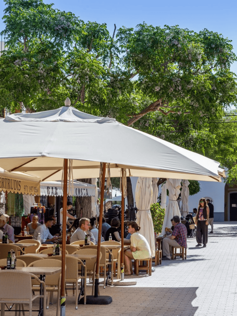 AlF text: Outdoor cafe with seating and umbrellas under lush green trees.