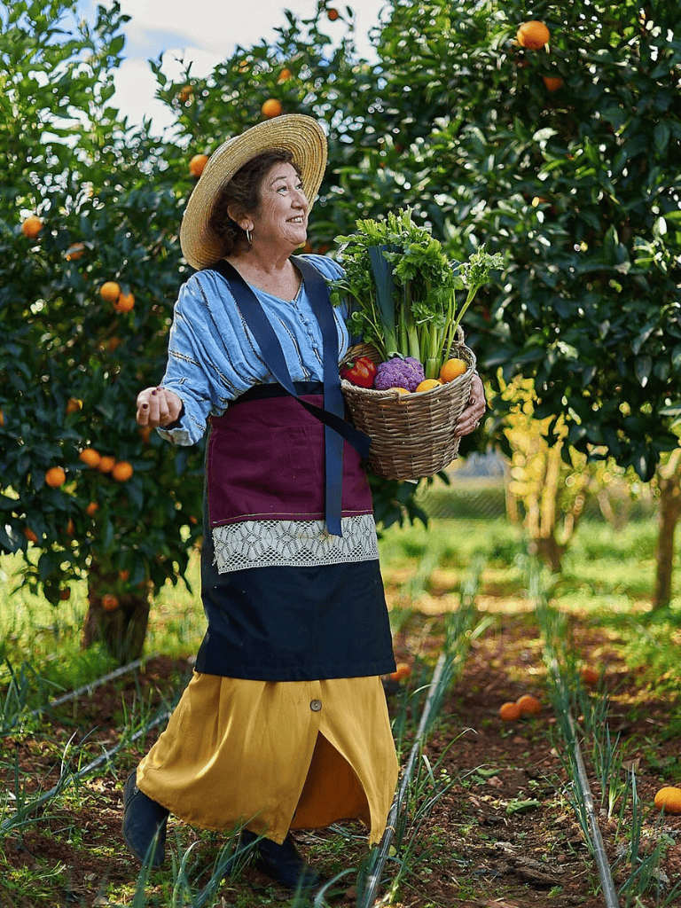 Vibrant woman harvesting fresh vegetables and oranges in orchard, enjoying farm-to-table experience.